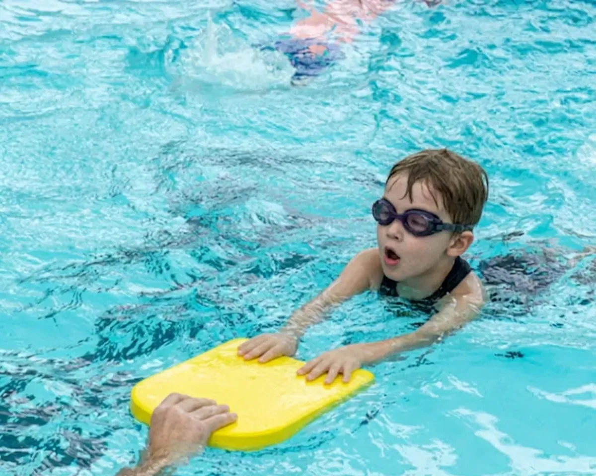 Kind mit Schwimmbrille übt mit Kickboard im Wasser